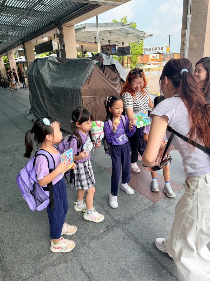 Preschool children showing off craft activity cards outside Beach Bazaar on Sentosa during a childcare family day