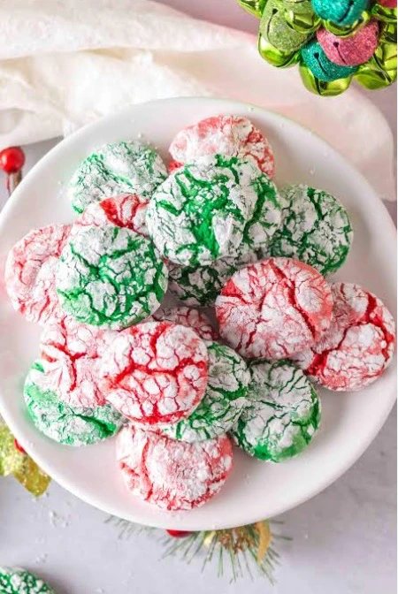 Red and green crinkle cookies dusted with icing sugar, piled on a white plate