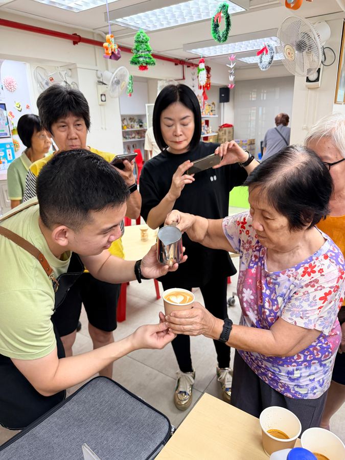 Senior receiving a heart latte art coffee from a barista trainer during the Seniors Barista Workshop
