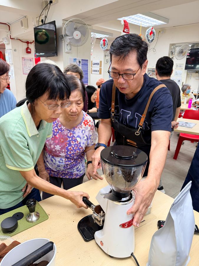 Seniors learning to use an espresso grinder and tamper with guidance from a barista trainer