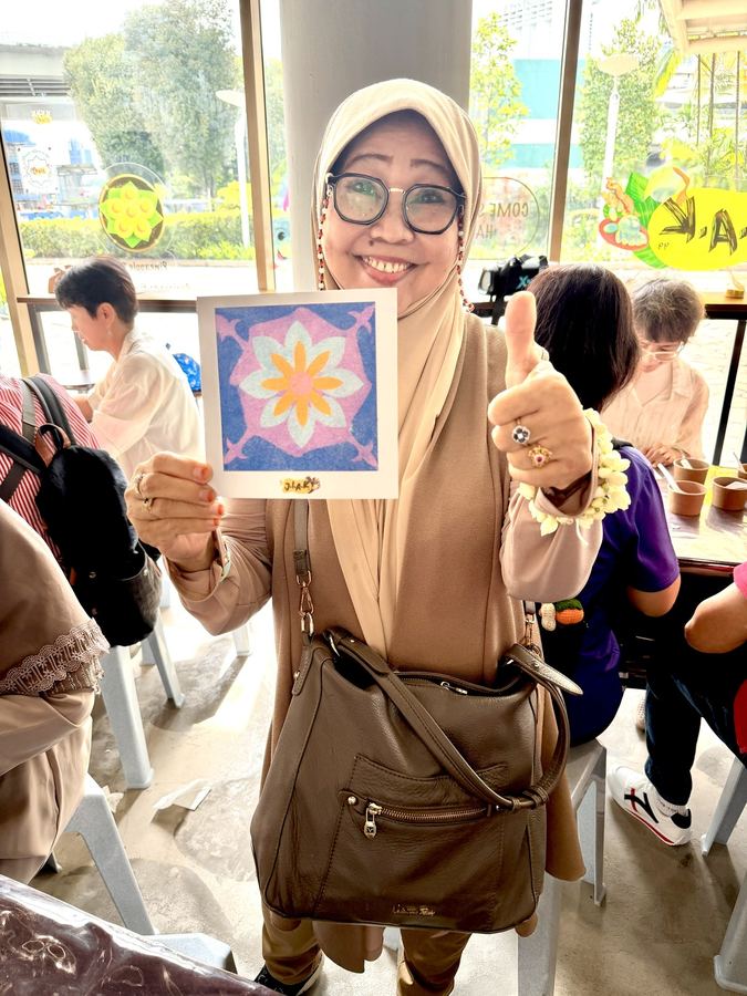 Senior proudly showing her handmade Peranakan sand art craft at JIAK99