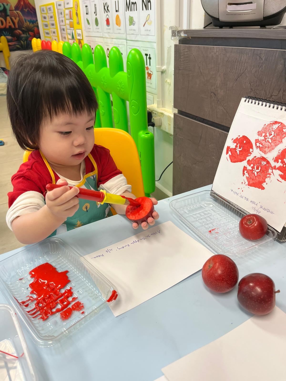 A toddler painting an apple half for star-stamp printing during art and science time