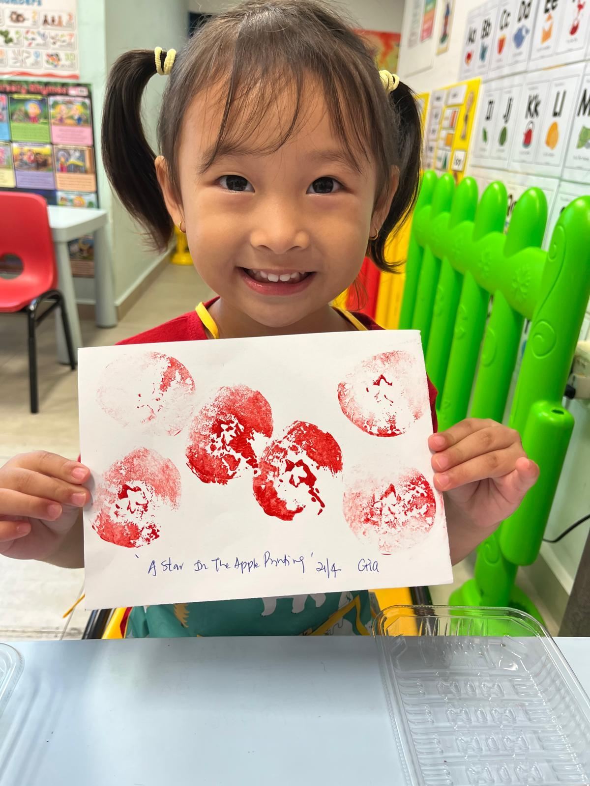 A smiling Star Tots girl proudly holding up her apple-print painting
