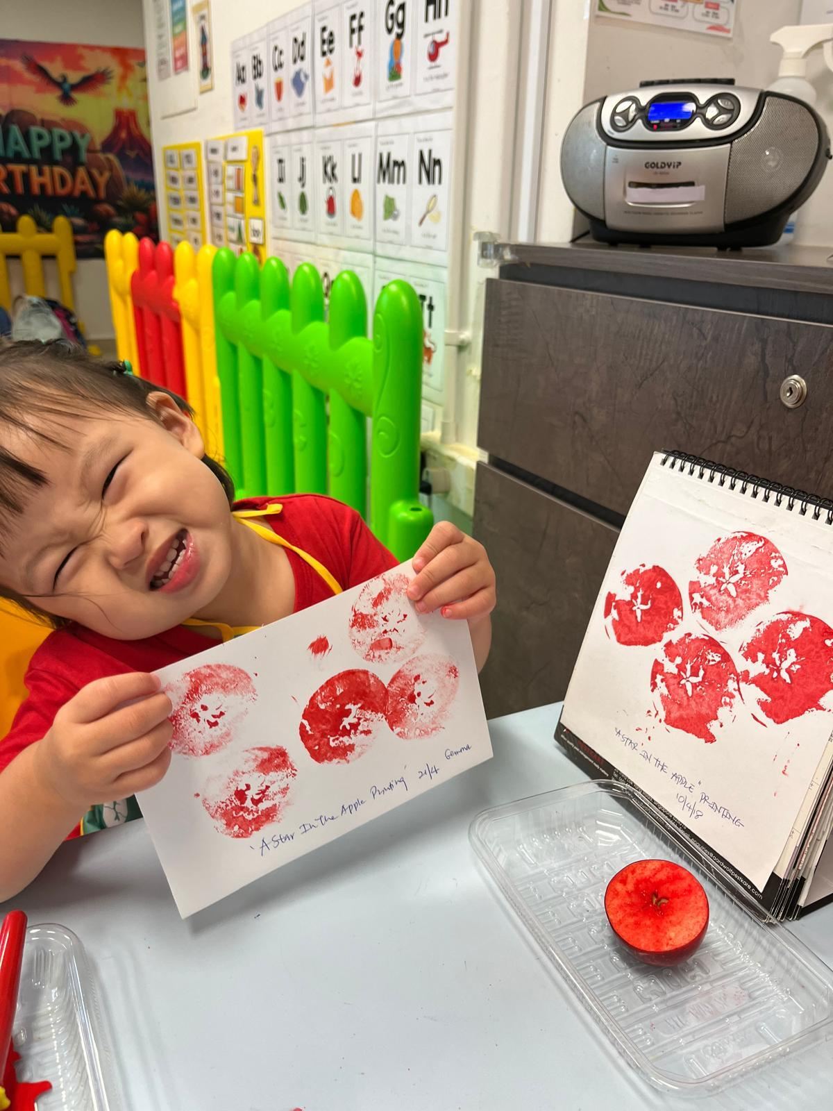 A delighted Star Tots child showing off her apple-print artwork