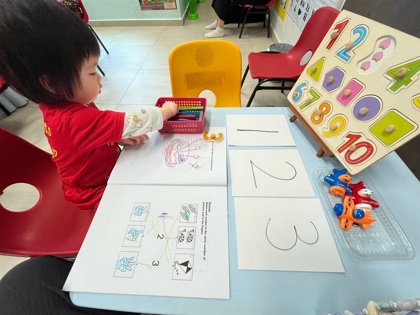 A Star Tots toddler practising numbers 1, 2, 3 with worksheets and a wooden number puzzle